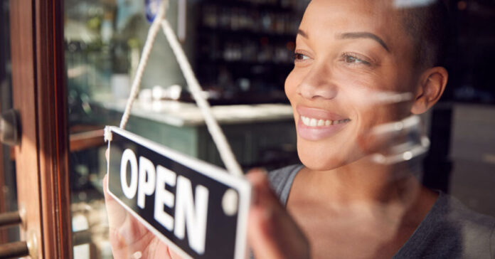 A woman displays an open sign in front of her store